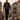 A giant model in a croc-texture zip jacket, red leopard shirt, and rhinestone pants walks through a miniature London, with double-decker buses and a "Barocco" sign.